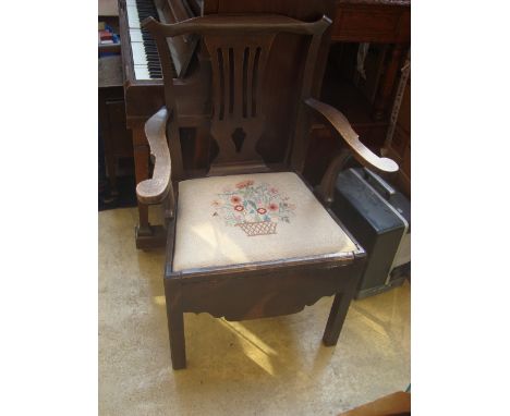 A George III oak Chippendale commode chair, with shaped crest rail and pierced back splat, open arms with scroll terminals on
