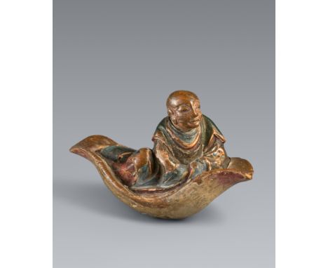 Netsuke eines Mönchs auf einem Lotosblatt. Nadelholz, farbig bemalt. 18./19. Jh.Ein in weite Roben gehüllter Mönch sitzt läss