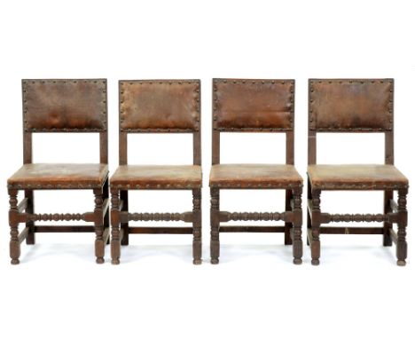 A set of four oak chairs, early 20th c, in Charles I style, the padded back and stuffed over seat covered in brass nailed hid