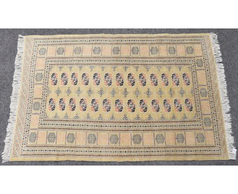 An Indian Bokhara rug of light yellow ground featuring two central rows of ghuls surrounded by multiple wide &amp; narrow bor