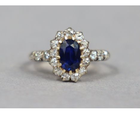 An early 20th century sapphire &amp; diamond ring, the oval centre stone weighing approx. 1 carat, set within a border of sma