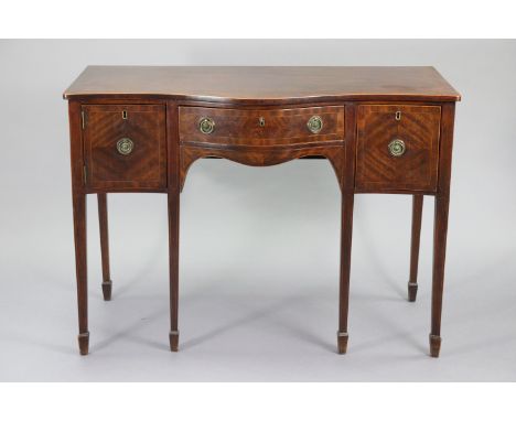 A Georgian inlaid mahogany serpentine-front sideboard fitted with a cupboard &amp; deep drawer either side of the central fri