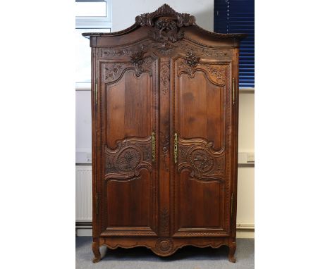 An 18th century carved oak armoire with an arched cornice centred by a wreath, billing doves, quivers, etc. above a central s