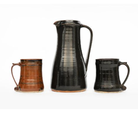 ‡ Leach Pottery a stoneware jug, tapering cylindrical form with applied handle, covered to the foot with a rich tenmoku glaze