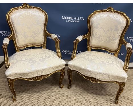 A pair of circa 1900 carved giltwood framed armchairs in the Louis XV taste with floral carved top rails over a moulded main 