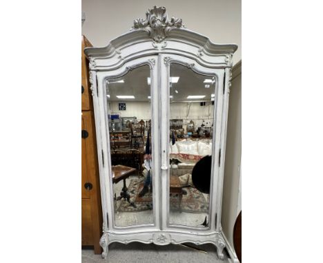 A French white painted armoire in the Louis XV style, the moulded and carved cornice over two bevel edged mirrored doors open