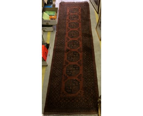 A Bokhara runner, the central panel set with repeating medallions on a dark red ground, within a red and black stepped border