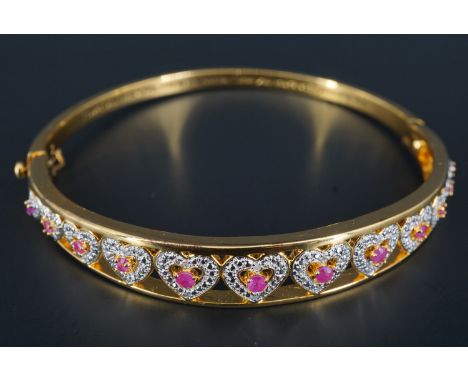 A contemporary ruby and gilt metal hinged bracelet, the rubies set on graded heart shaped fields between converging bars, 62 