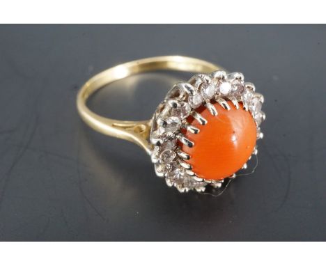 A coral, diamond and 18 ct gold cluster ring, the coral cabochon of approx 7 mm crown set within a frame of small diamond bri