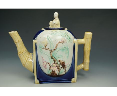 A late Victorian Majolica teapot, body formed as a round set into a square, decorated in relief decoration of a bird and butt