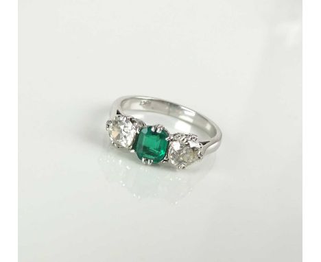 A three stone emerald and diamond ring, designed as a central octagonal-oval cut emerald flanked to each side by an old cut d