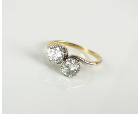 A two stone diamond crossover ring, the brilliant cut diamonds claw set in white metal to yellow metal shank, stamped '18ct',