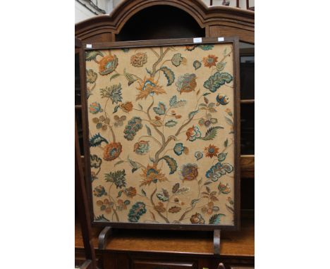 An early 20th Century oak firescreen, the embroidered panel depicting flowering foliage on a beige ground