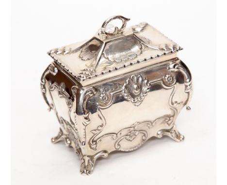 An Edwardian silver bombe shaped tea caddy, chased with scrolling foliage and shells, the hinged cover with scroll handle, on