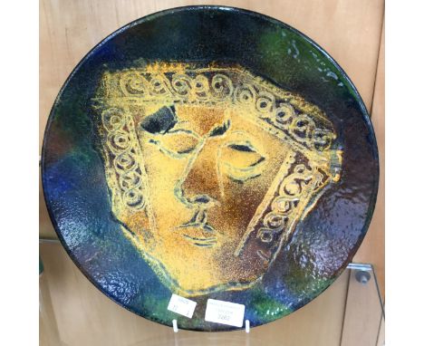 A Circular metal enameled plaque. Art Deco stylised mask in yellow, on green ground.