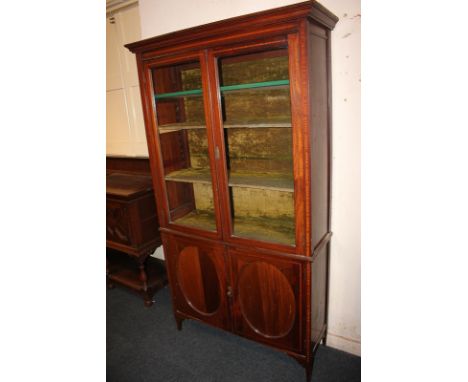 An Edwardian inlaid mahogany bookcase with two glazed panel doors enclosing three shelves, on cupboard base enclosing shelf, 