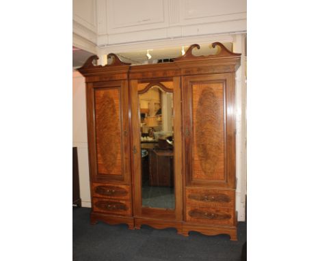 A large inlaid mahogany triple wardrobe, possibly French, with double swan neck pediment above a central mirrored door, flank