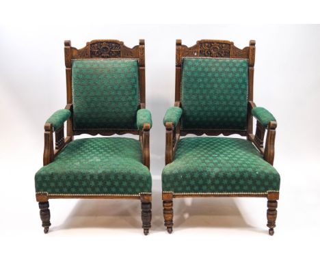 A pair of late Victorian armchairs with carved mahogany frames, upholstered in green on turned legs and ceramic casters