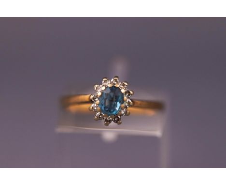 A yellow metal cluster ring set with an oval blue topaz surrounded by diamonds. Hallmarked 9ct gold. Size K. Weight: 1.9 gram