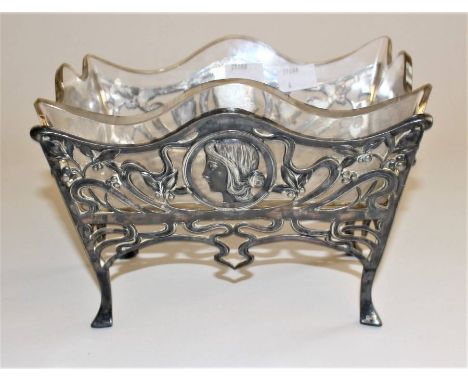 An Art Nouveau WMF table centrepiece cast with profile female heads and pierced tendrils on scroll feet, clear cut glass line