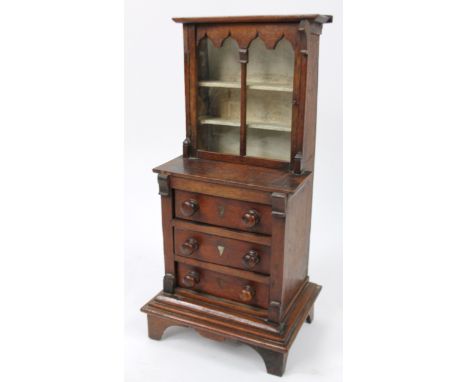 A miniature or tradesman's oak table top bookcase, the upper section with overhanging top above a hinged glazed door, the sub
