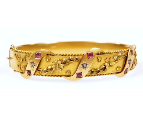 An Edwardian 9ct gold ruby and diamond bangle, partially set with flowerheads and ribbon design, 7cm wide. (in fitted case)
