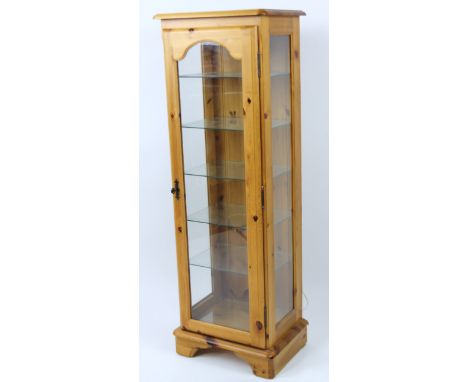 A Corndell stripped and lightly polished pine display cabinet, with three part glazed case on overhanging base terminating in