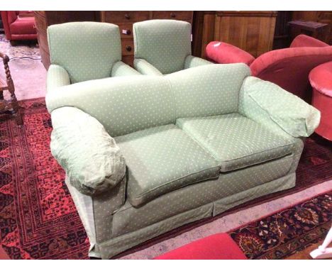 A two seater sofa with concave back above scroll arms, green upholstery with multiple stylised flowerheads, on bun feet termi