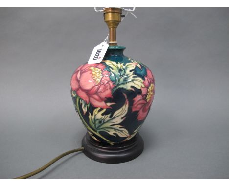 A Moorcroft Pottery Table Lamp, painted in the 'Peony' pattern against a dark blue ground, mounted on a wooden base, with sha