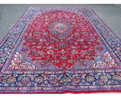 A LARGE CARPET WITH RED CENTRAL GROUND AND BLUE BORDER, APPROX 360 X 270 CM - WEAR THROUGHOUT