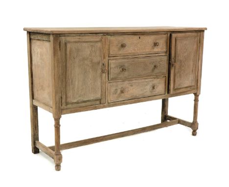 A Cotswold School oak sideboard, after a design by Heal &amp; Sons, with a central stack of three drawers, each with panelled