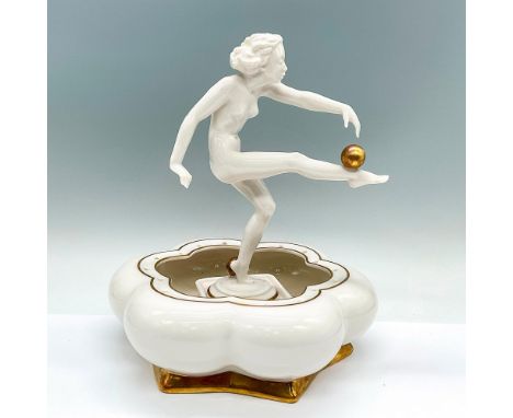 A white nude figure, also known as Sun Worshipper. She is balancing a gold orb on her leg. Incudes a floral shaped white bowl