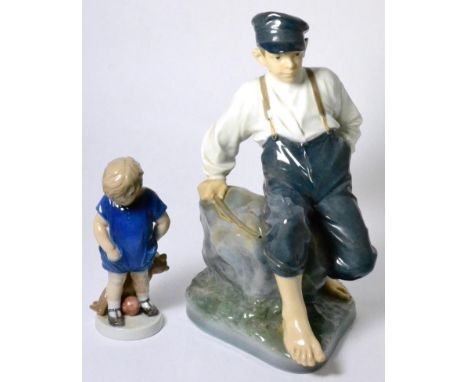 A large Royal Copenhagen porcelain model of a boy seated on a rock; and a small model of a young boy holding a teddy bear (2)