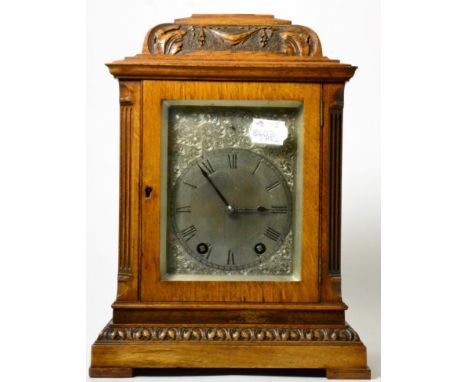 An oak striking carved mantel clock, circa 1910, inverted pediment, side sound frets, silvered dial with Roman numerals, twin