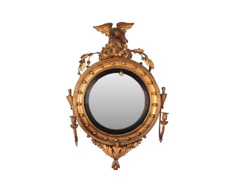 A Regency giltwood convex girandole mirror, with circular plate within ebonised frame, surmounted by an eagle on a rockwork c