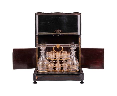 A Victorian ebonised serpentine-fronted decanter box and glasses, the cover with inlaid brass decoration and monogram, the hi