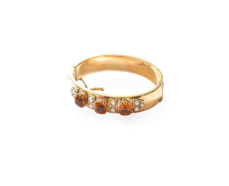 A 9 Carat Gold Citrine and Split Pearl Bangle, three cushion cut citrines in yellow claw settings, spaced by pairs of split p