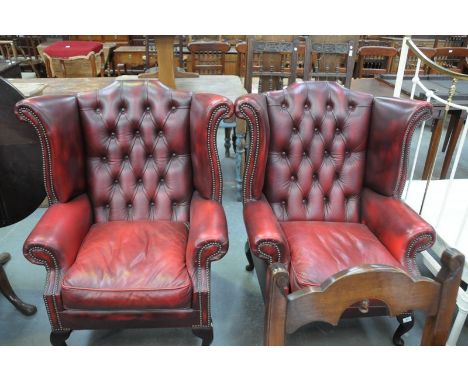 A Pair of ox blood red leather button back and wing back fireside armchairs.