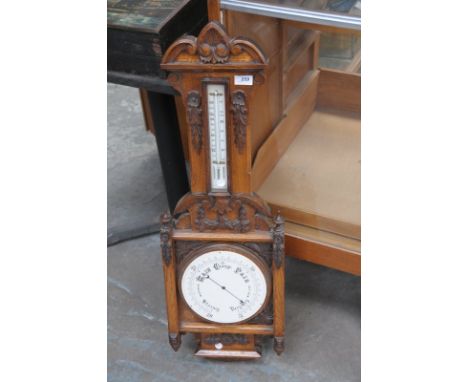 A Victorian carved oak wall barometer and thermometer with a white enamelled dial the case embellished with leafy swags. 