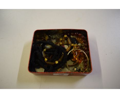 A tin containing a gold plated bangle, an amber coloured pendant, and various jewellery 