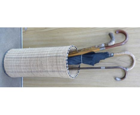 Three walking canes, two silver mounted and a silver mounted Paragon umbrella in a wicker stick stand