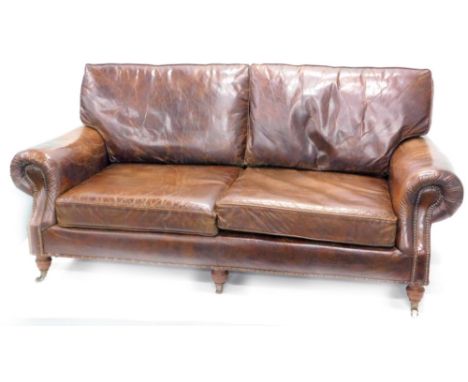 A brown distressed type leather sofa, with two added back and seat cushions, Chesterfield type arms, with brass studs on turn