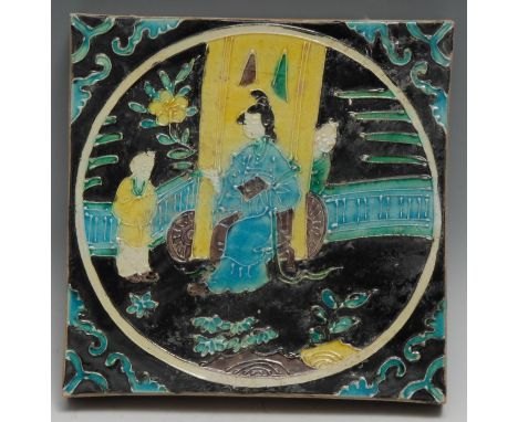 A Chinese tile, decorated in relief with a lady of the court and her attendants, glazed in tones of yellow, green, brown and 