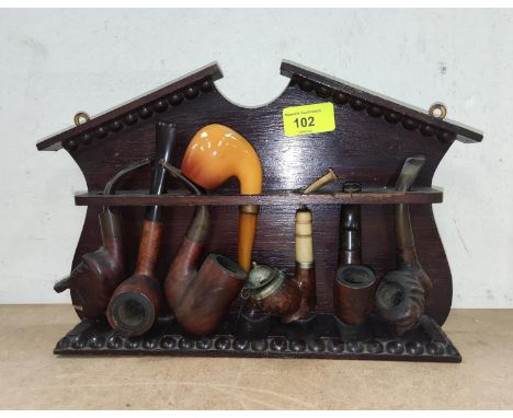 An oak pipe rack with a selection of carved and other pipes. 
