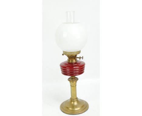 A Victorian brass and glass oil lamp with ruby glass reservoir, opaque white glass shade and clear chimney, raised on circula