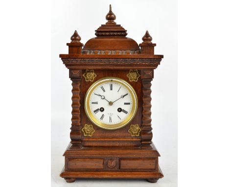 A 20th century mahogany mantel clock with carved stepped top with three finials, ornamental pilasters either side of the whit