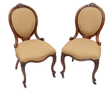 A pair of Victorian walnut spoon back side chairs, each with carved top rail, oval padded cameo back, padded stuff-over seat 