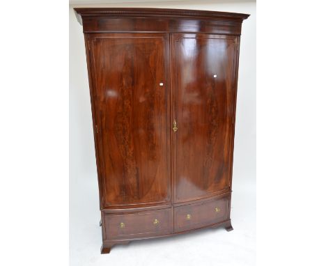 An Edwardian mahogany slightly bow front wardrobe with two hinged doors with oval crossbanded panels enclosing hanging space 