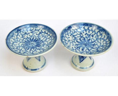 A pair of 19th century Chinese stem cups, painted in underglaze blue with flower head on scroll ground within cloud border to