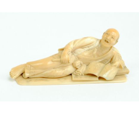 A Japanese Meiji period ivory okimono modelled as a reclining gentleman reading a book, signed to base, length 9cm.   CONDITI